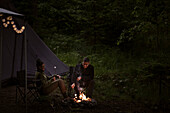 Couple camping in forest and sitting by campfire