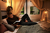 Man reading book on bed in camper van