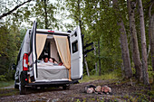 Women lying in bed in camper van parked in forest
