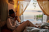 Woman sitting in bed in camper van and drinking tea