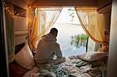 Mann sitzt im Wohnmobil und schaut auf den See