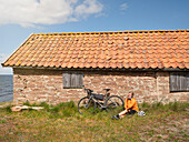 Radfahrer entspannt sich in der Nähe eines Steinhauses am Meer