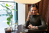 Frau im Restaurant, die mit dem Handy telefoniert und die Zeit überprüft