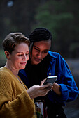 Lächelndes weibliches Paar benutzt Smartphone im Freien