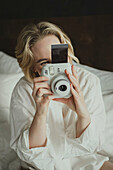 Blond woman photographing in bedroom