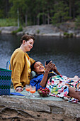 Weibliches Paar beim Picknick am Fluss und beim Telefonieren