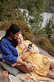 Female couple having picnic and using phone