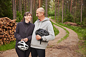 Smiling couple holding bike helmets in forest