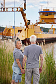 Senior couple holding hands and looking at industrial barge