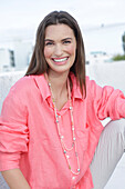 Young woman in salmon coloured shirt with pearl necklace and light coloured trousers