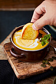 Dipping bread in creamy pumpkin soup with pumpkin seeds