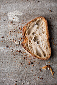 A slice of farmhouse bread with crumbs on a grey background