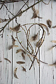 Heart made of budded twigs and feather on wooden table
