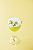 A green cocktail garnished with dill (Gin Sour)