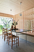 Dining area in front of window front and wooden slatted wall, custom built bench with storage space