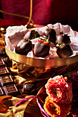 Mit Schokolade überzogene Erdbeeren in Pralinenschale davor Blumen