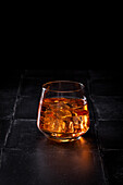 A glass of whisky with ice cubes against a black background