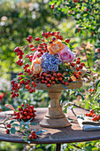 Autumn flower arrangement with roses, hydrangeas and rose hips on wooden stand