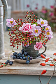Herbststrauß mit Hagebutten, rosa Rosen und Herbstanemonen in Tasse