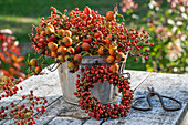 Rose hip branch in zinc bucket in front of autumn wreath of rose hip berries