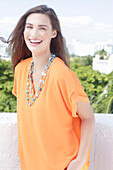 A cheerful young woman wearing an orange summer blouse with a necklace