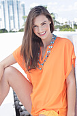 A cheerful young woman wearing an orange summer blouse with a necklace