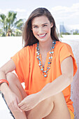 A cheerful young woman wearing an orange summer blouse with a necklace