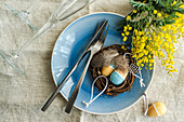 Tischdekoration mit kleinem Osternest und leuchtend gelben Mimosenblumen auf Betontisch