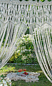 View through macramé curtain on picnic blanket with drinks in the garden