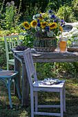 Sommerlicher Blumenstrauß mit Sonnenblumen, Kugeldisteln, großer Bibernelle, Bienenfreund, Oregano und Kosmeen auf Holztisch im Garten