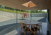 Round table with classic chairs in front of a floor ot cieling glass wall in an architect's house