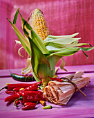 Still life with corn on the cob, corn leaves, and red chilies
