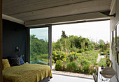 Doppelbett mit gelber Tagesdecke im Schlafzimmer mit Gartenblick durch offene Glastür