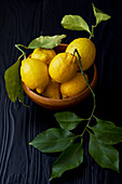 Fresh lemons with leaves in a wooden bowl