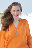 Young, blond woman in orange blouse in good mood on the beach