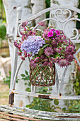 Bouquet of starflower, hydrangea, and phlox in vase hung on garden chair