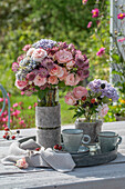 Bouquets of roses with hydrangeas and blackberry branches in vases with felt cuffs on a patio table