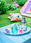 Glasvasen und Laterne auf Holztisch im Sommergarten