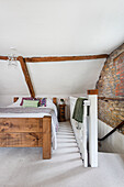 Doppelbett im Dachgeschoss-Schlafzimmer mit Holzbalken, Sichtmauerwerk und Treppenabgang