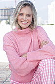 A young blonde woman wearing a pink turtle-neck jumper and checked trousers