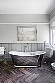Freestanding bathtub in metallic look with mirror above in a bathroom with wood-look floor tiles