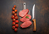 Raw beef tenderloin steak on wooden board with cherry tomato branch