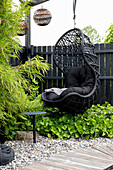 Black rattan hanging chair with cushions in the Asian-style garden area