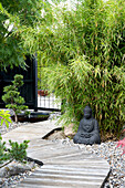 Zen garden with winding wooden walkway, Buddha statue and bamboo