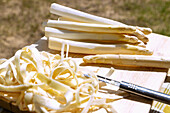White asparagus, peeled, with a peeler on a wooden board outside