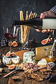 Male hand pouring wine in stemmed glass set54 on table with cheese, charcuterie and fruit