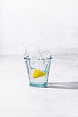 Lemon creating a splash in a small glass of water.