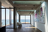 Minimalistischer Wohnraum mit Sofa und modernem Kunstwerk and der Wand, Blick auf das Meer