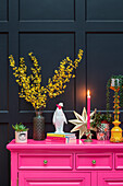 Colourful sideboard with decorations and plants against a dark wall