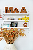 Wall shelf with letters and decorative objects above bouquet of dried flowers